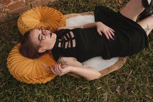 Figure in dark clothing lies on grass with an orange circular pillow beneath their head.
