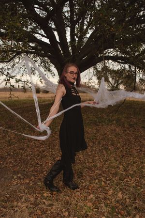 A figure in dark clothing dances with flowing white fabric among autumn leaves on the ground.