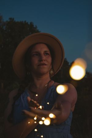 A silhouetted figure in a hat gazes up at glowing bokeh lights against a dark evening sky.