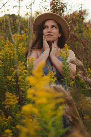 A dreamy portrait in a field of golden wildflowers with a person wearing a wide-brimmed hat gazing upward.