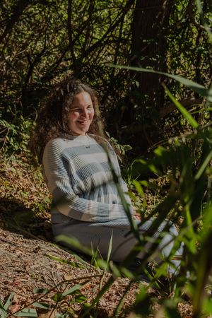 Person in a striped sweater sits among autumn foliage during an outdoor photoshoot.