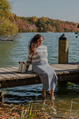 Person in a cozy sweater relaxes on a wooden dock by a serene lake during fall.