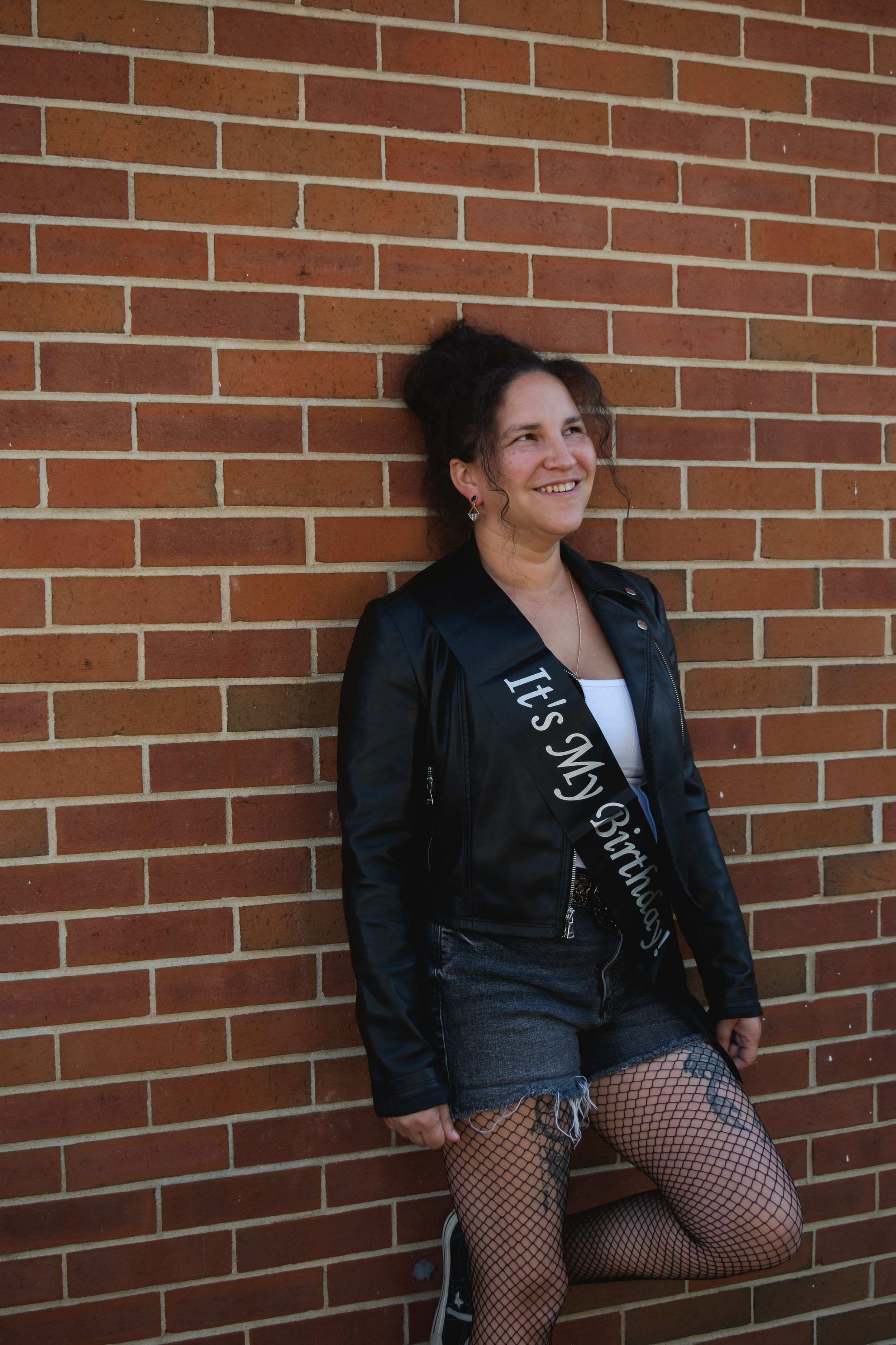 A series of photos against a brick wall showing someone in a black jacket and fishnet stockings.