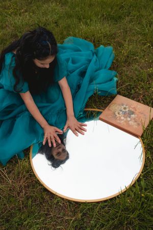 Someone wearing teal clothing uses white powder or flour to create patterns on a circular wooden surface outdoors.