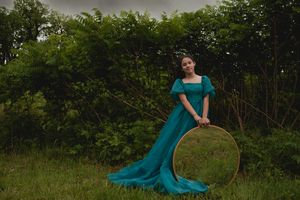 A woman in a flowing teal dress poses gracefully in a lush garden setting at sunset.