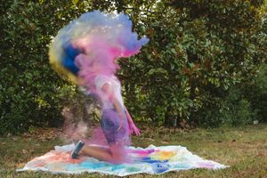 Colorful powder explodes in a vibrant cloud during an outdoor photo session against a natural green backdrop.