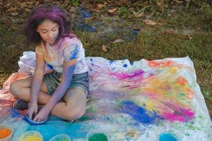 A colorful tie-dye painting session on a large white canvas outdoors during a summer activity.