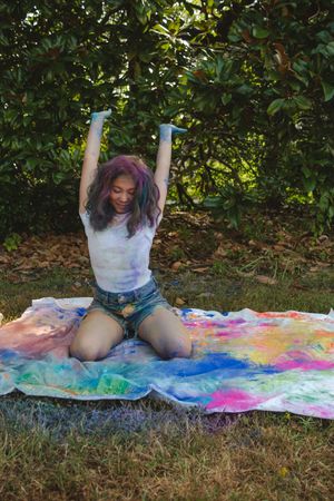 A series of five photos showing someone creating colorful tie-dye art on fabric outdoors on grass.