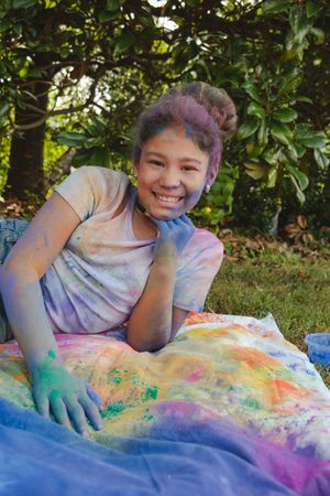 A colorful powder paint play session outdoors shows hands covered in vibrant hues of pink, blue and yellow.