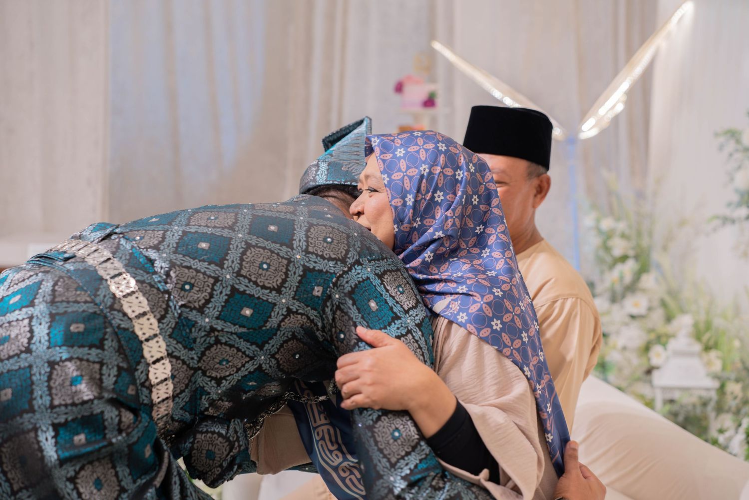 An emotional embrace during a traditional ceremony with white floral decorations.