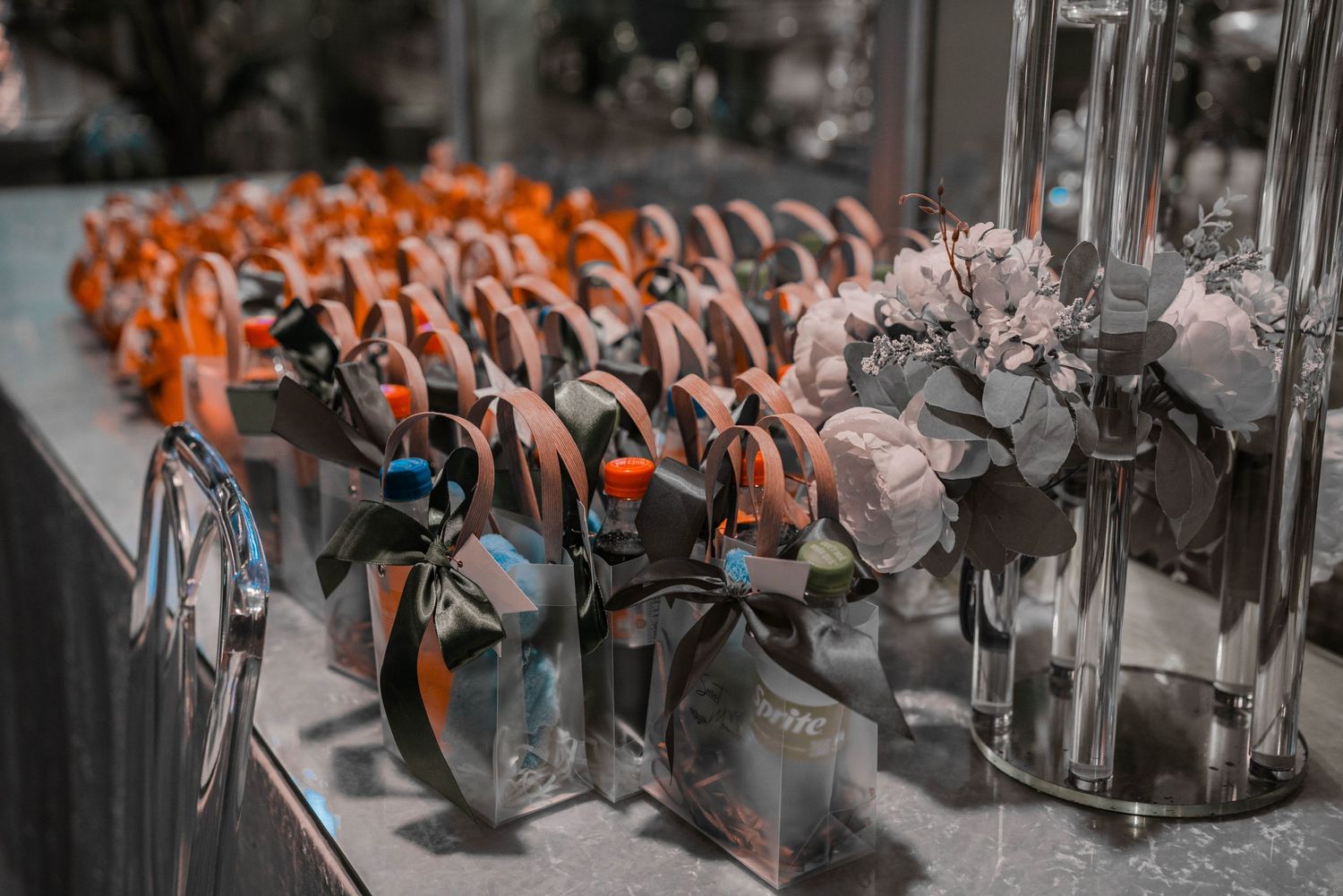 Wedding favors and decorative bottles lined up on a table with orange ribbons.
