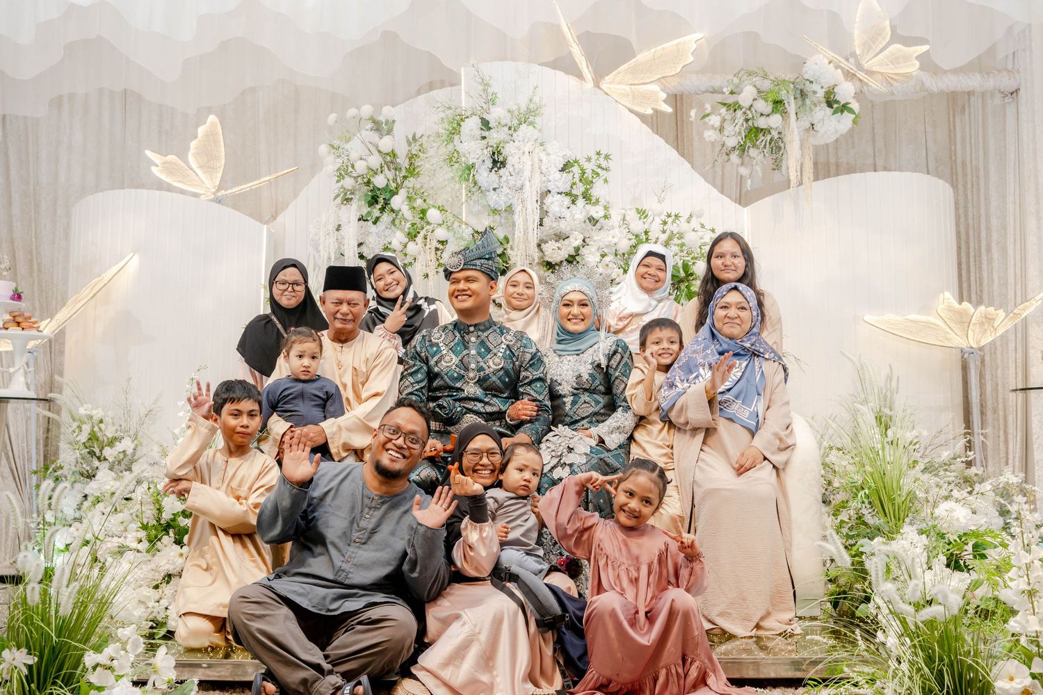 Large family group photo on decorated wedding stage with butterfly and floral elements.