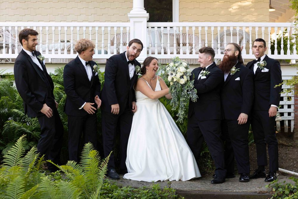 Wedding party gathered on porch steps in formal attire with black suits and white gown.