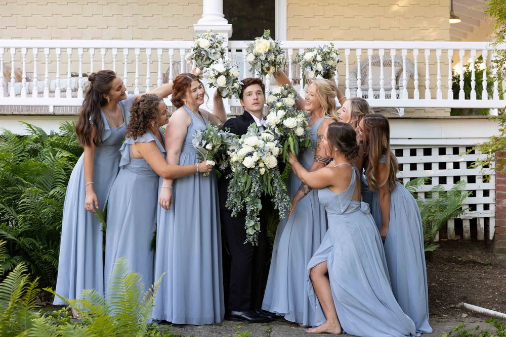 Wedding party in dusty blue dresses poses together on garden steps with white lattice backdrop.