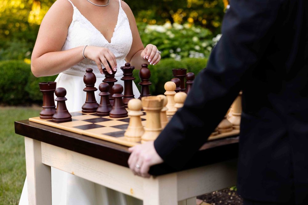 A wedding couple plays chess outdoors at a white table during their celebration.