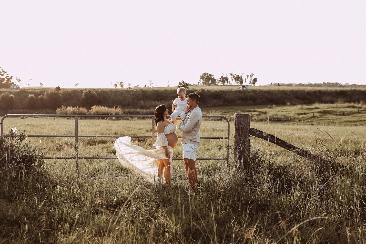 Family enjoying tender moment together by wooden fence in golden field.