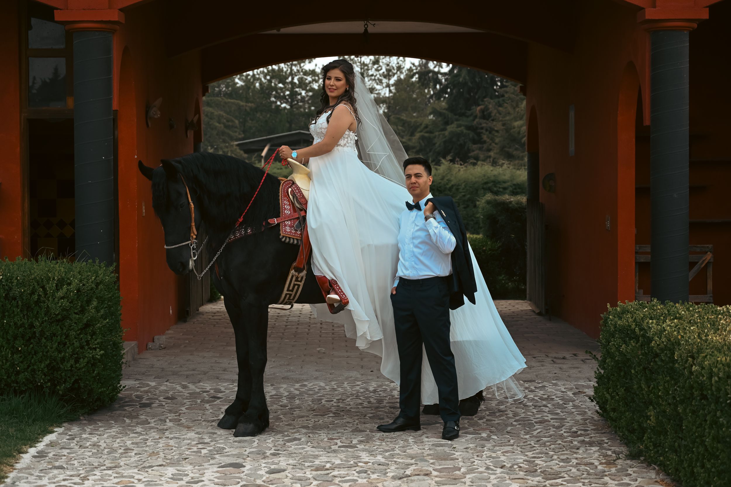 A wedding couple poses under a rustic wooden pergola with terra cotta roof tiles.