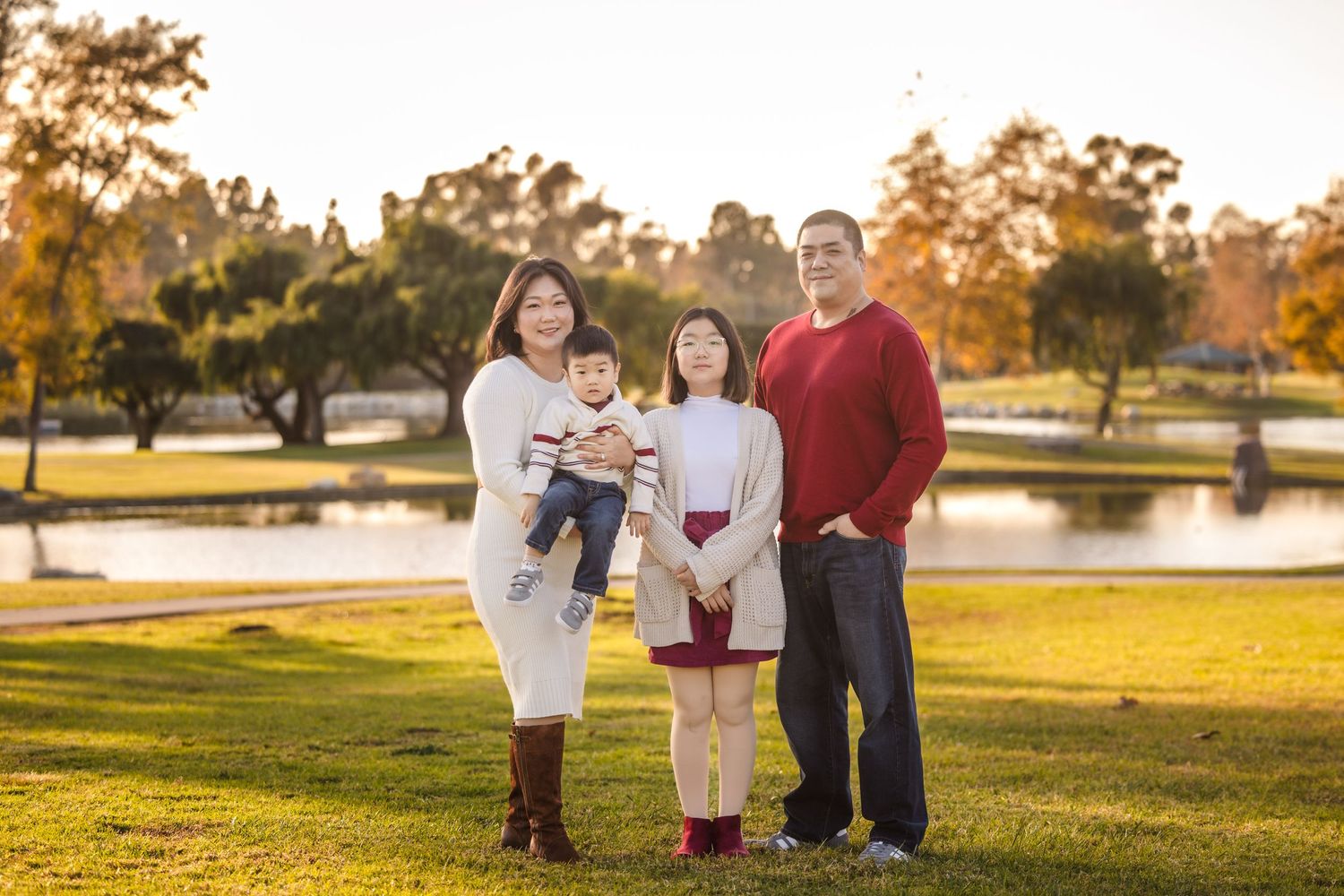 A family standing together on a grassy hill during golden hour sunset at a park with a pond in the background.