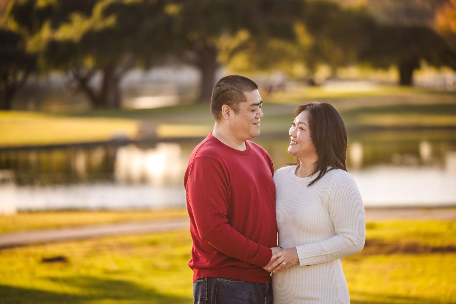 Couple shares an intimate moment at sunset in a park with golden light and a lake in the background.