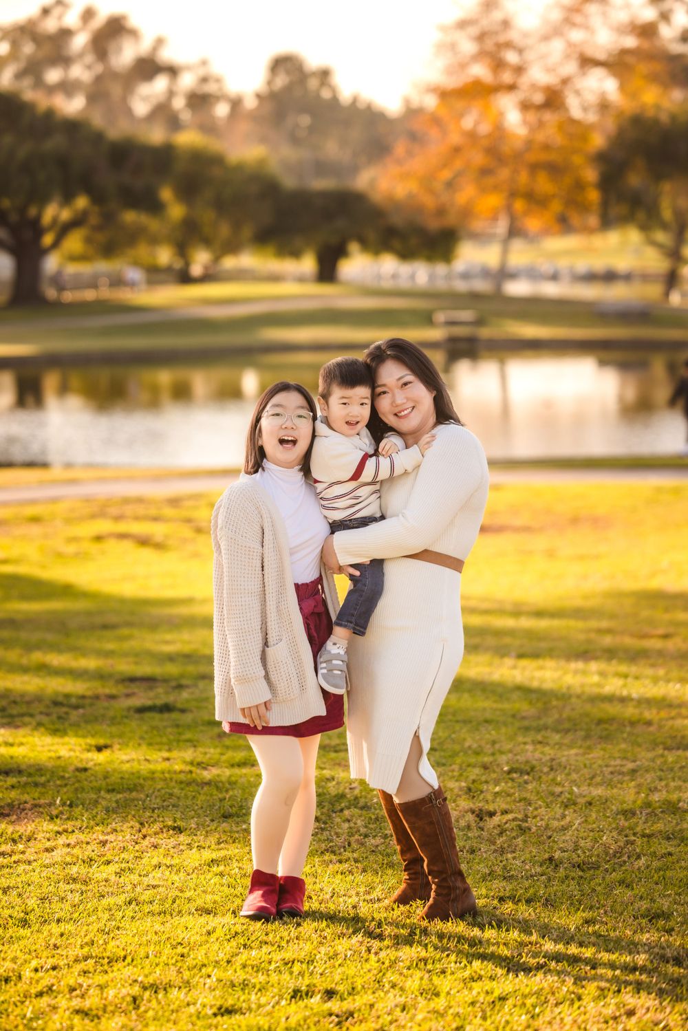 Family poses together at sunset by a lake in a park with golden autumn light on grass.