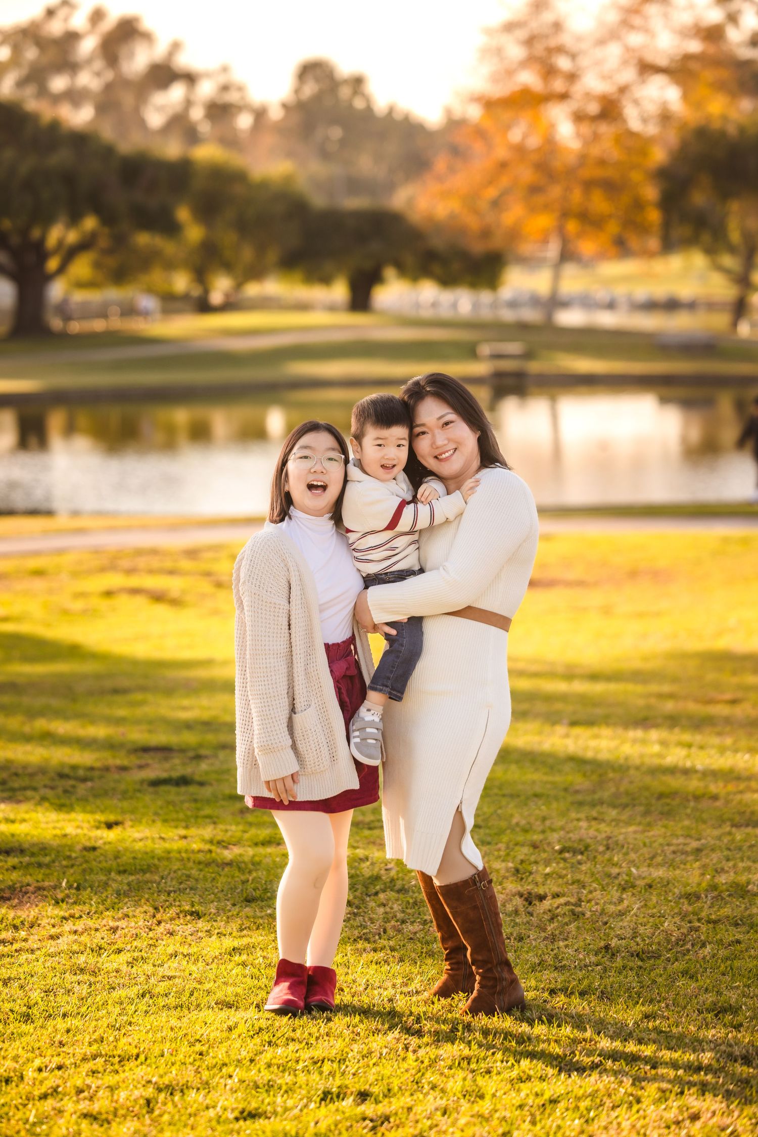 Family poses together at sunset by a lake in a park with golden autumn light on grass.