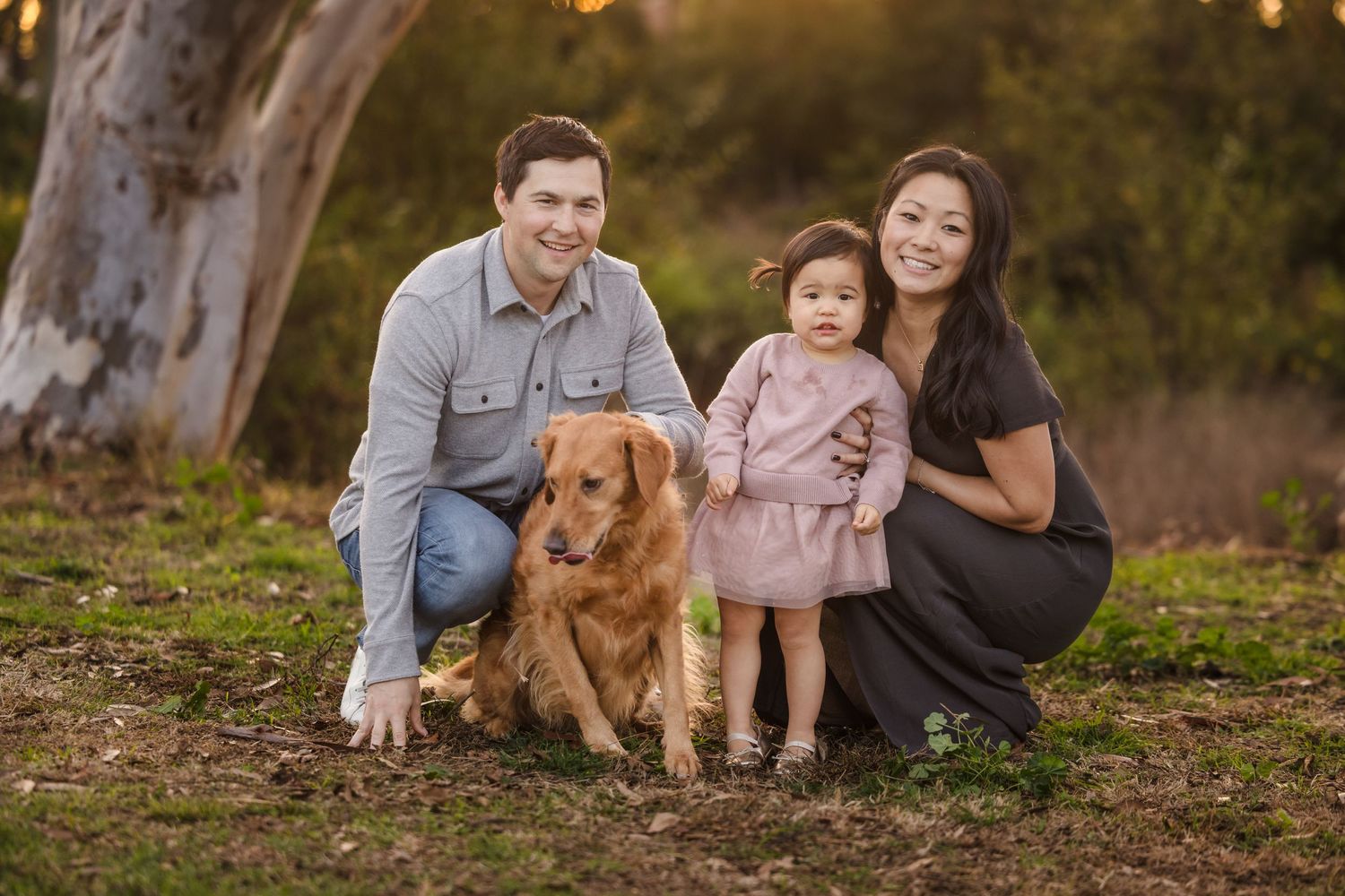 A family poses together with their golden retriever on a grassy slope during golden hour.