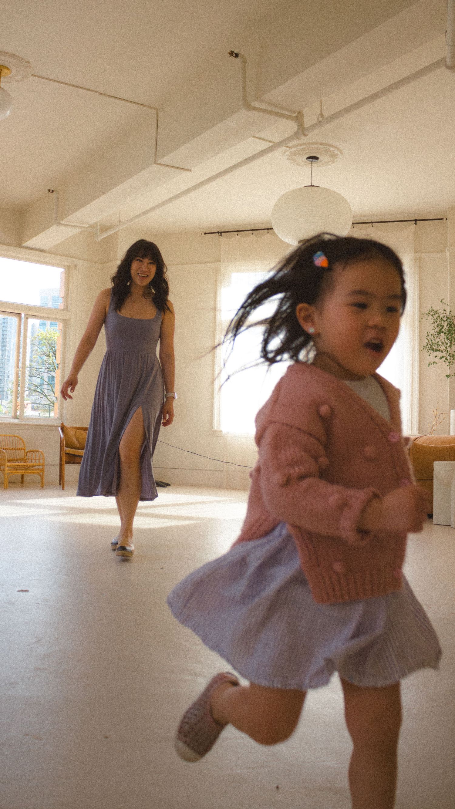 Toddler girl wearing pink and purple running away playfully from her mom during a studio motherhood session in Vancouver, BC.