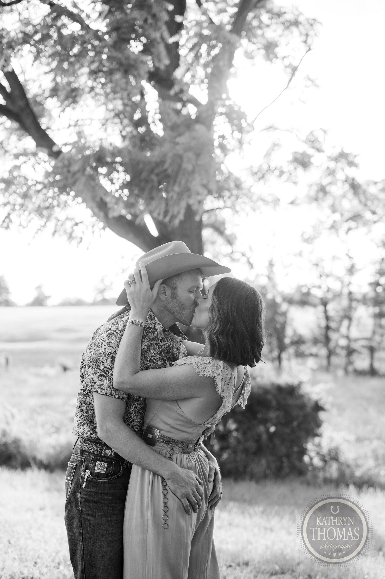 A romantic black and white photo of a couple embracing in a field at sunset.