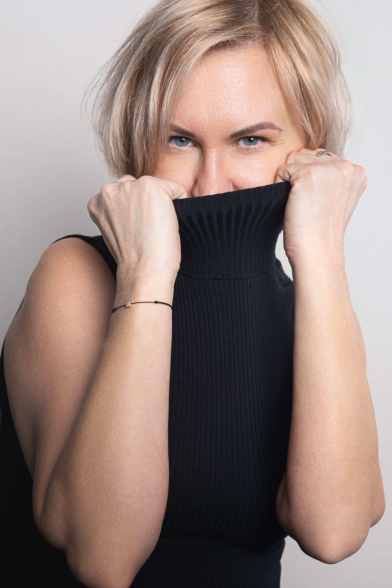 Playful portrait of person pulling up black turtleneck sweater.