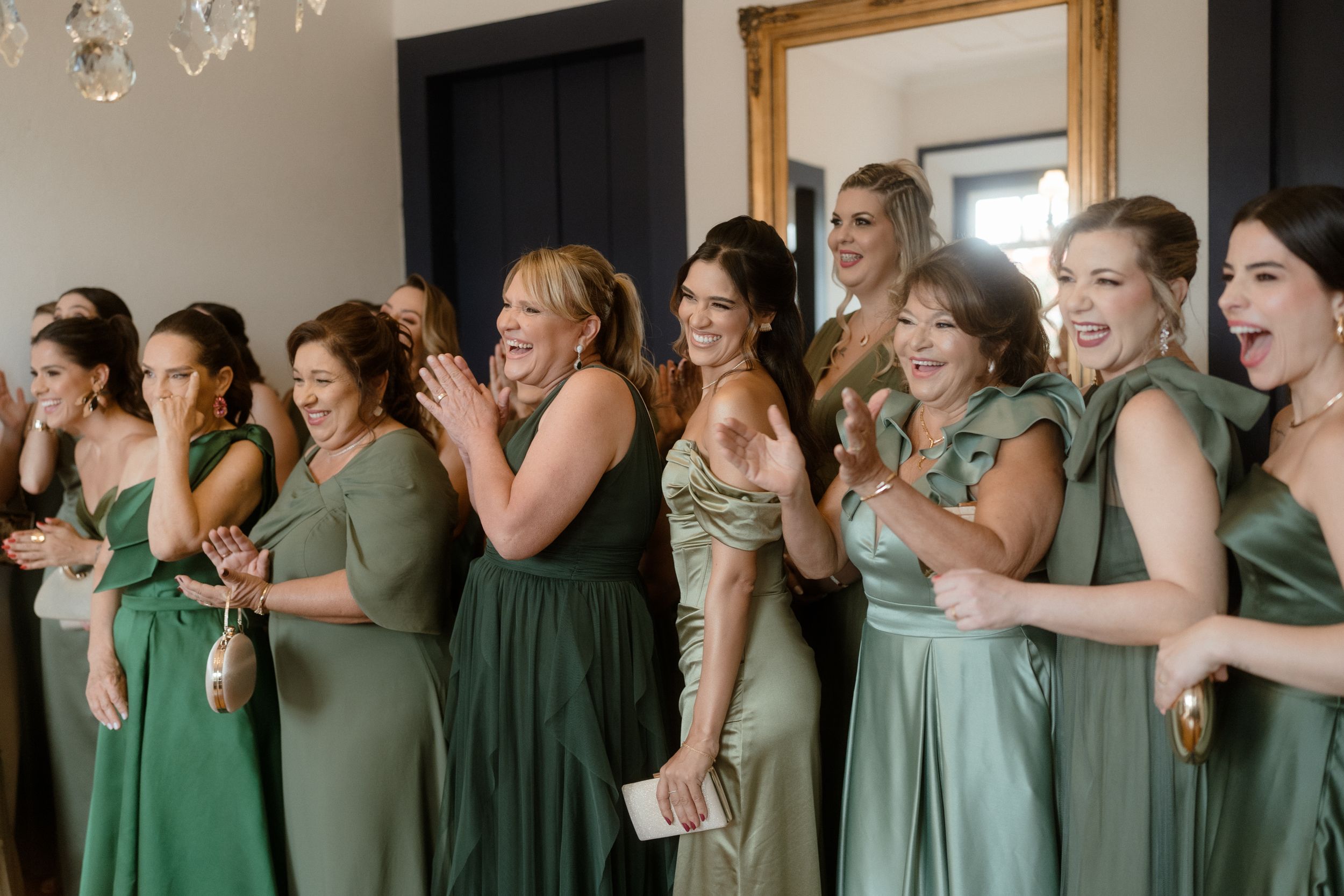 Wedding party wearing sage green dresses reacts with joy and excitement.