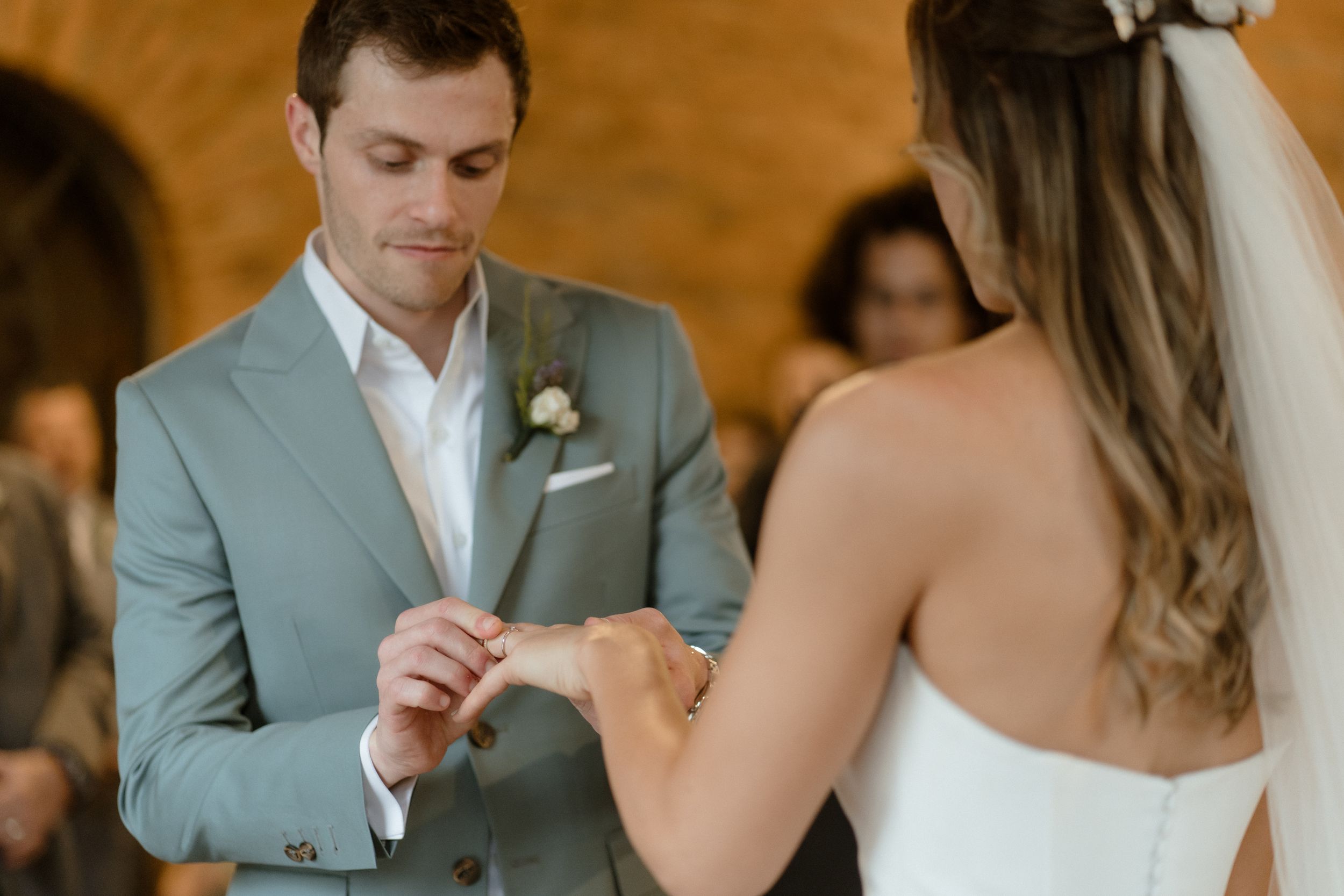 A tender ring exchange moment during an intimate wedding ceremony in a light-filled brick venue.