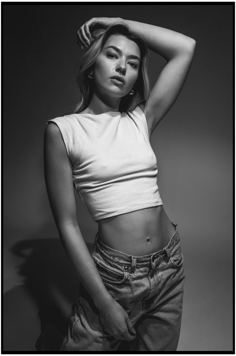 Dramatic black and white fashion photo featuring a cropped white top and high-waisted denim in moody lighting.