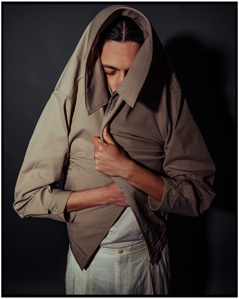 Dramatic portrait of person in beige jacket looking down in shadowy lighting. Portland portrait photographer
