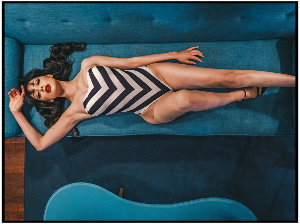 A fashion photo showcasing a black and white chevron swimsuit on a blue velvet couch. Portland portrait photographer