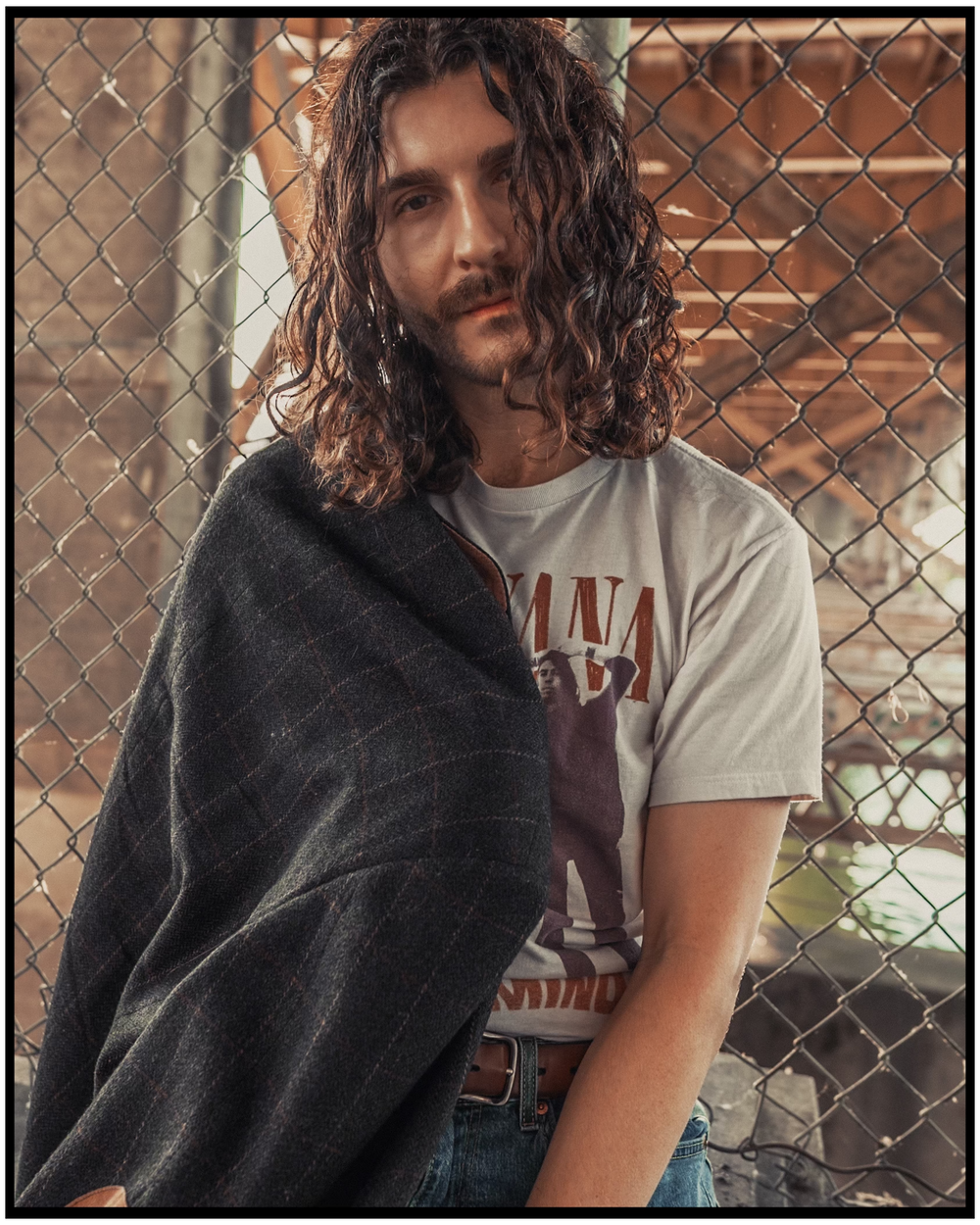 A moody portrait featuring long wavy hair and a vintage band t-shirt against a chain link fence background. Portland portrait photographer