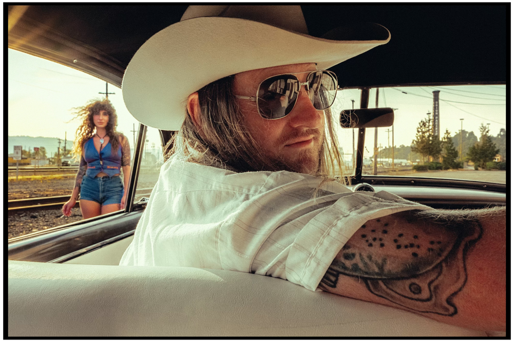 View through car windshield showing cowboy hat and tattoos with desert backdrop. Portland portrait photographer