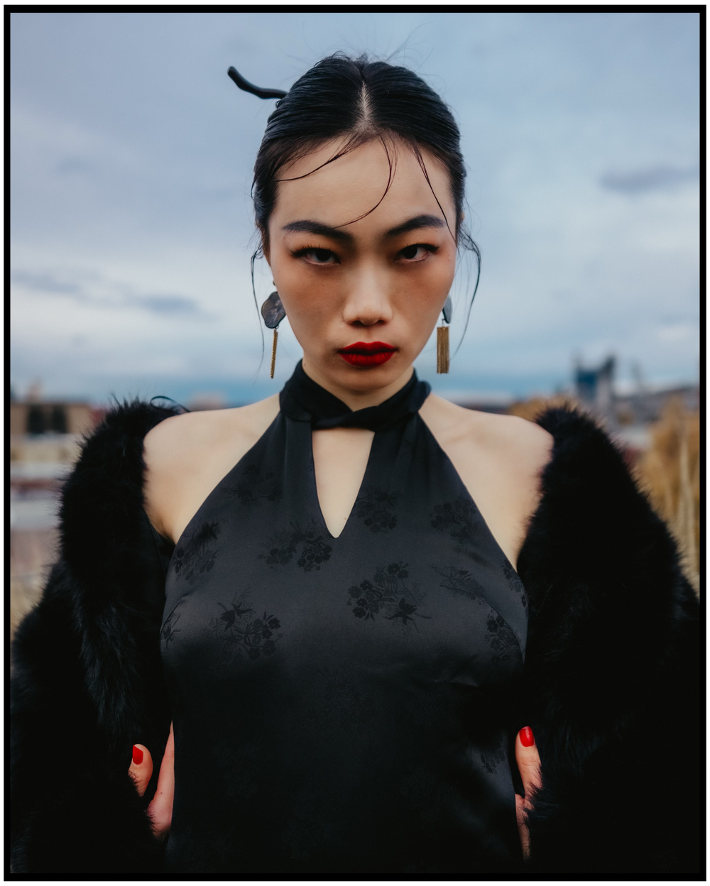 Person in black halter dress and fur shawl poses against cloudy sky. Portland portrait photographer