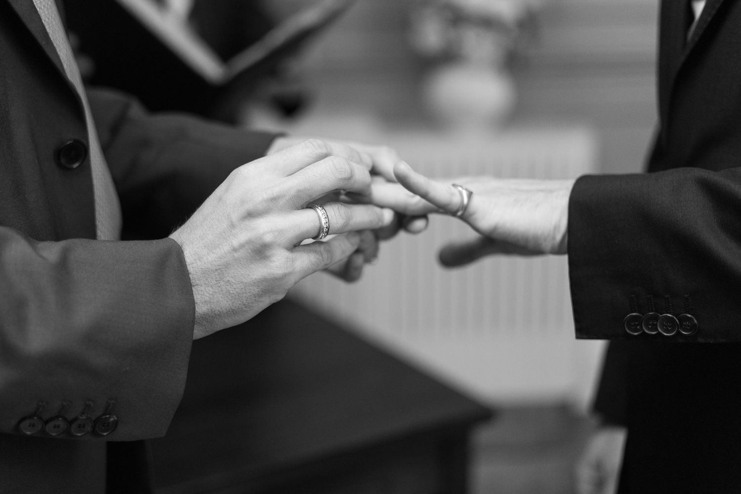 Close-up black and white shot of hands exchanging wedding rings during a ceremony.