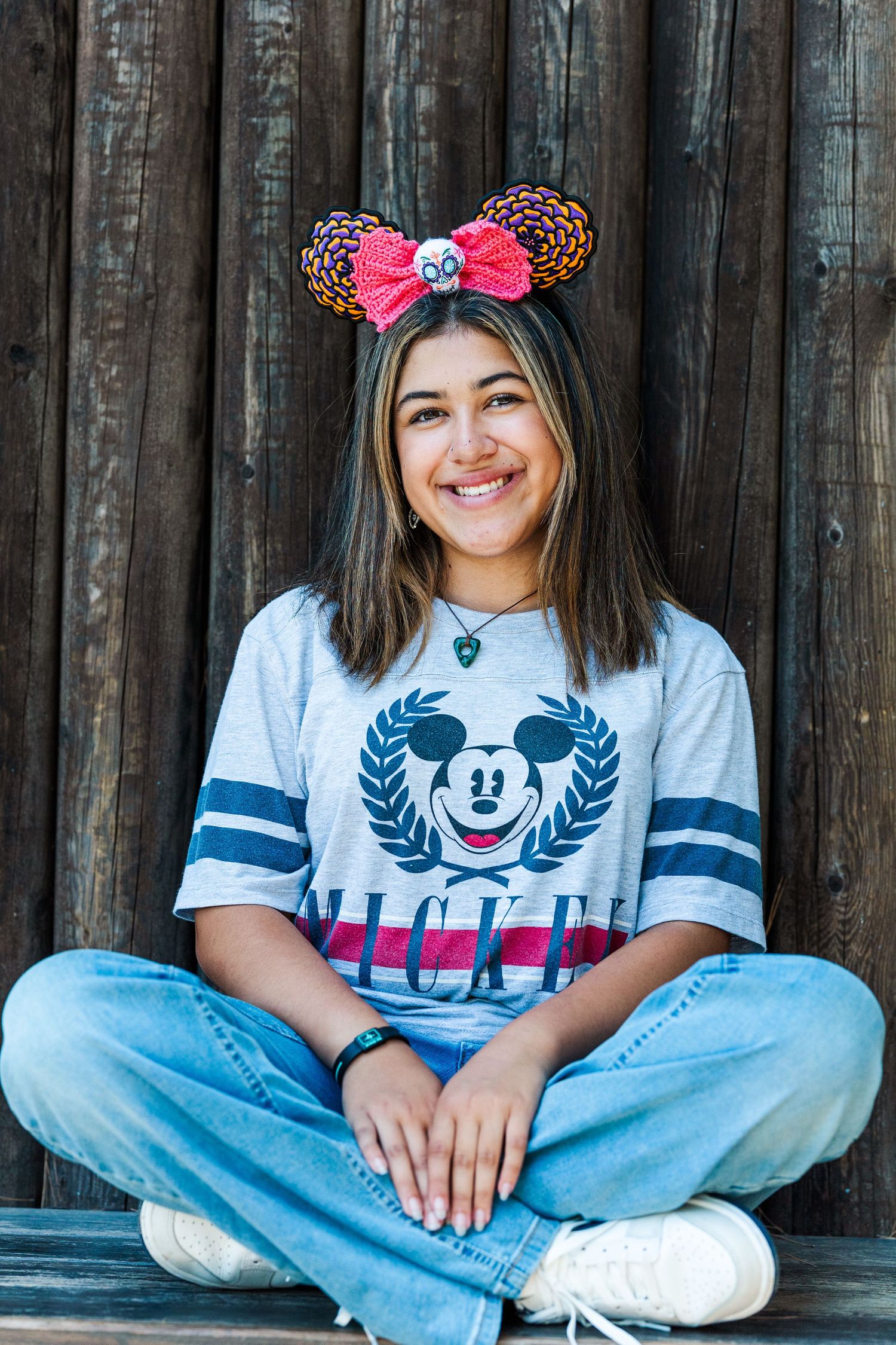 Person wearing Disney Mickey Mouse t-shirt and leopard print Minnie ears sits cross-legged against wooden wall.
