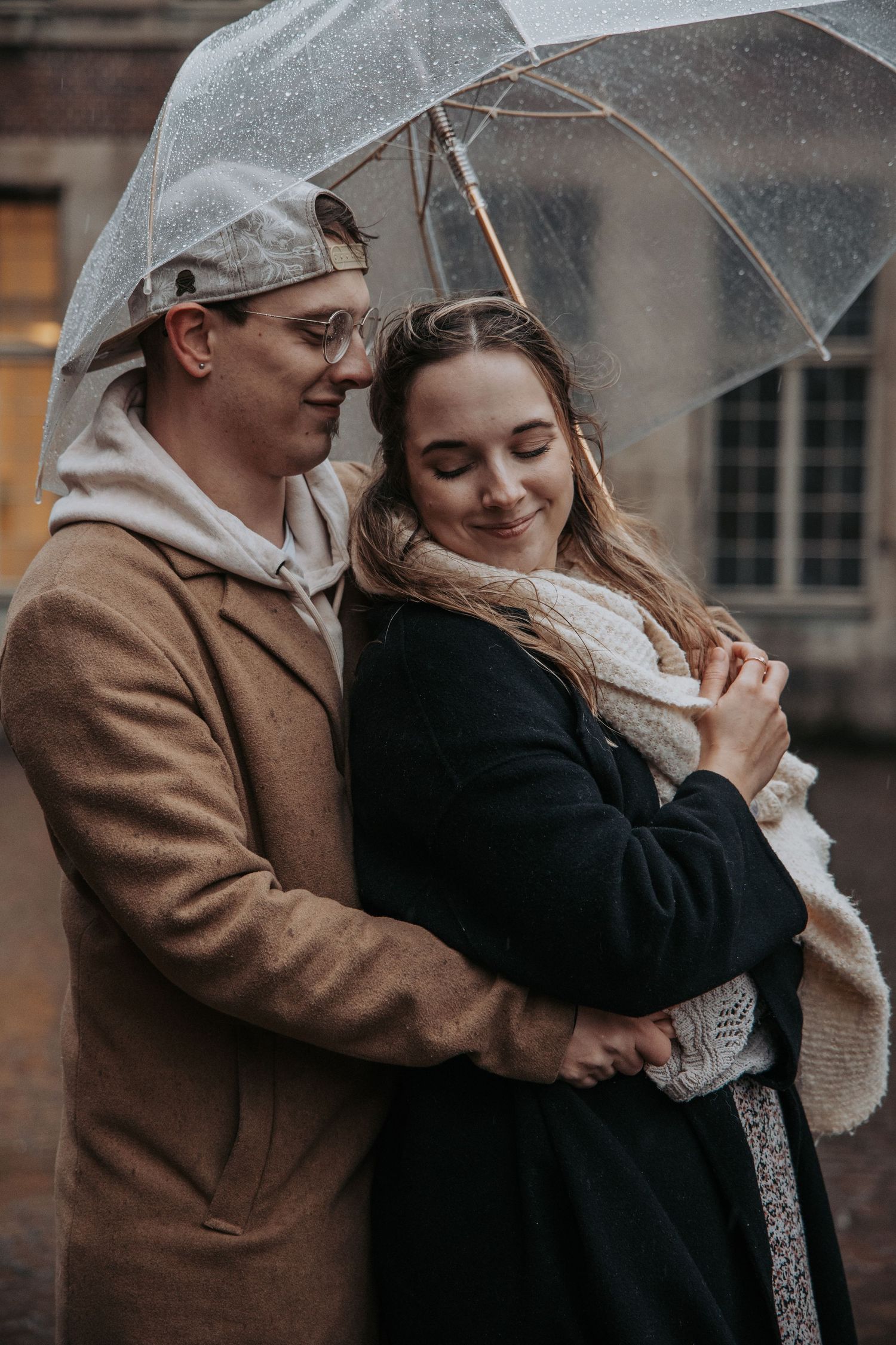 A romantic couple shares an intimate moment under a clear umbrella on a cloudy day.