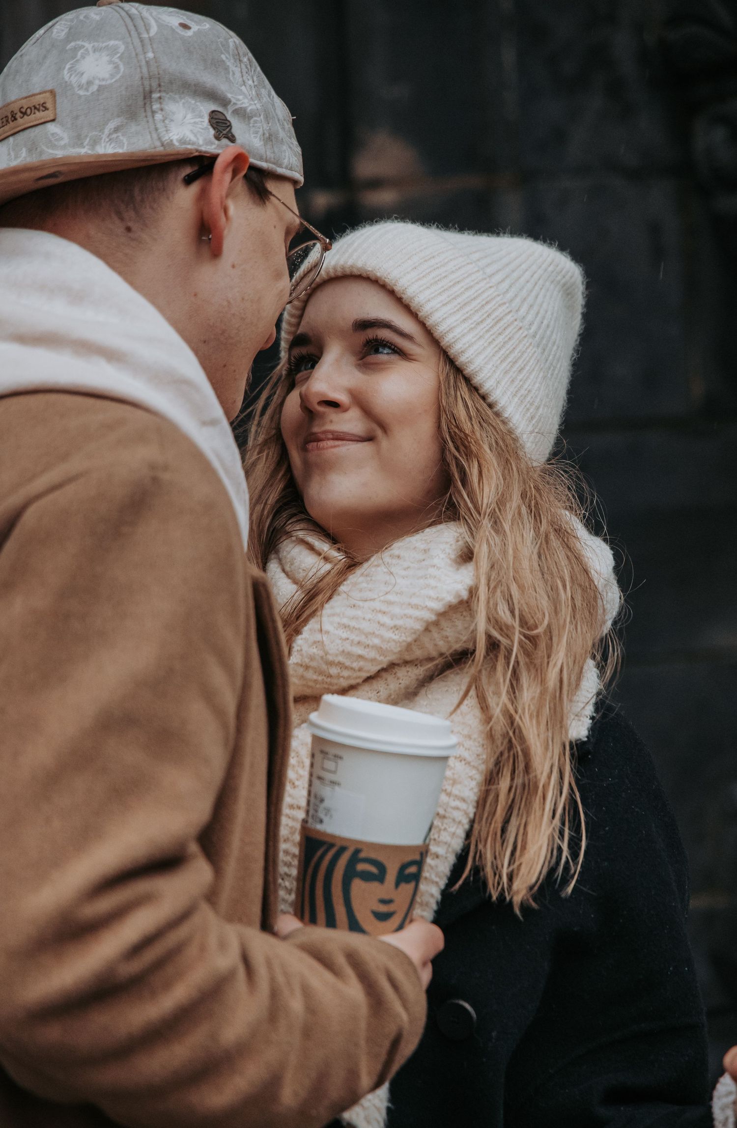 Couple in winter clothing sharing an intimate moment while holding coffee cups outdoors.