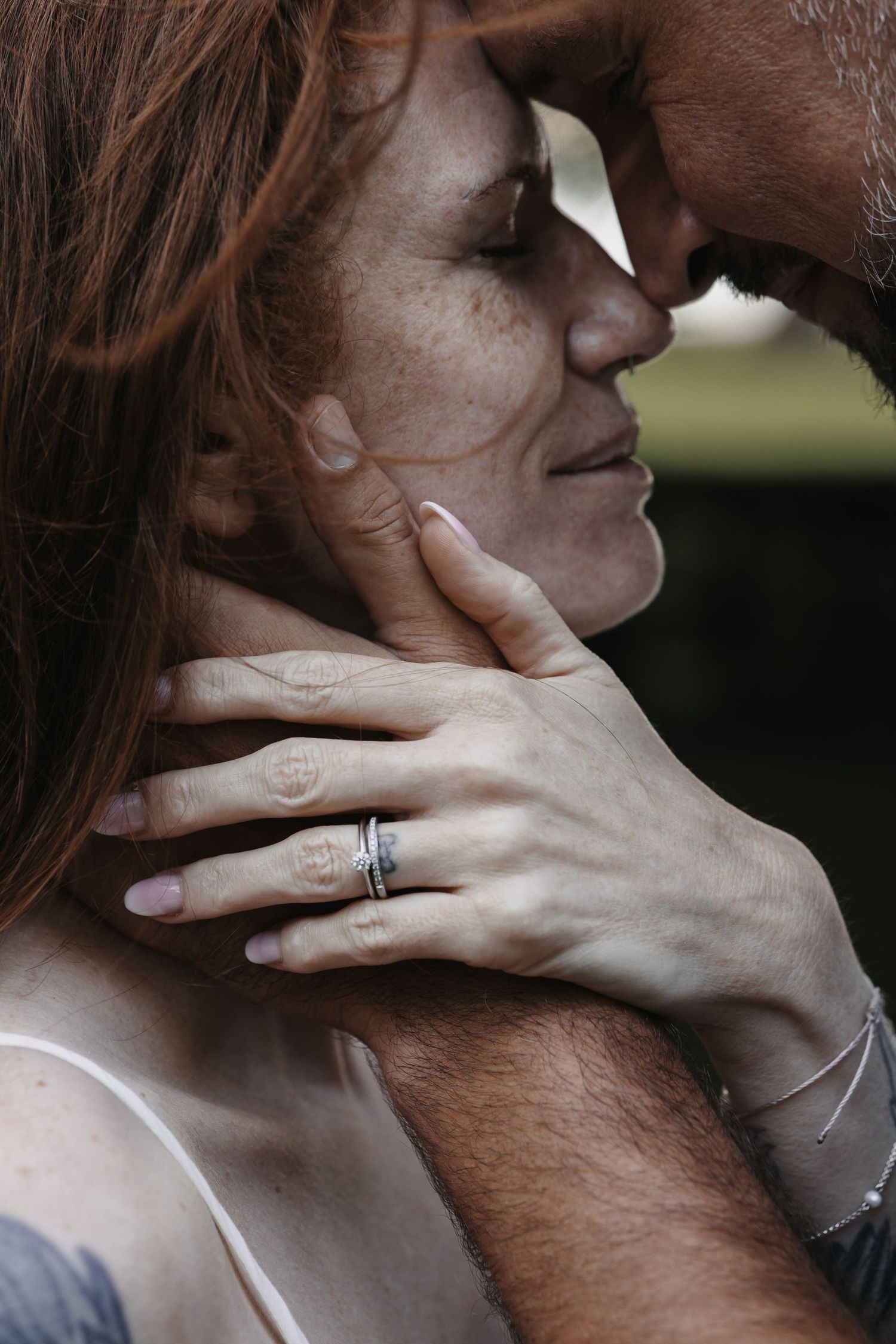 Intimate couple moment with redhead woman wearing rings, man tenderly holding her face as they lean in close together.