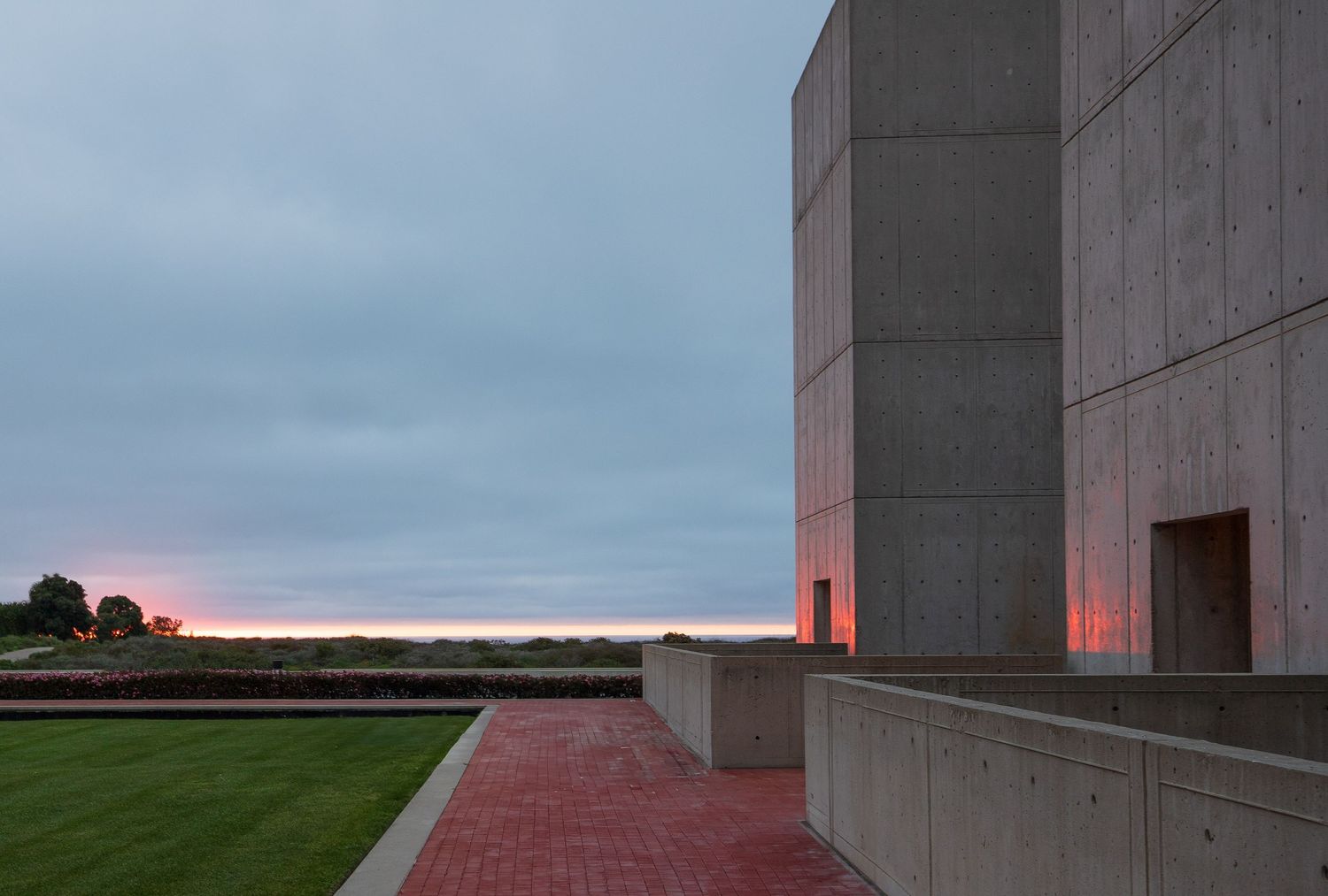 Modernist concrete building exterior at sunset with red lighting and geometric shapes at the Salk Institue.