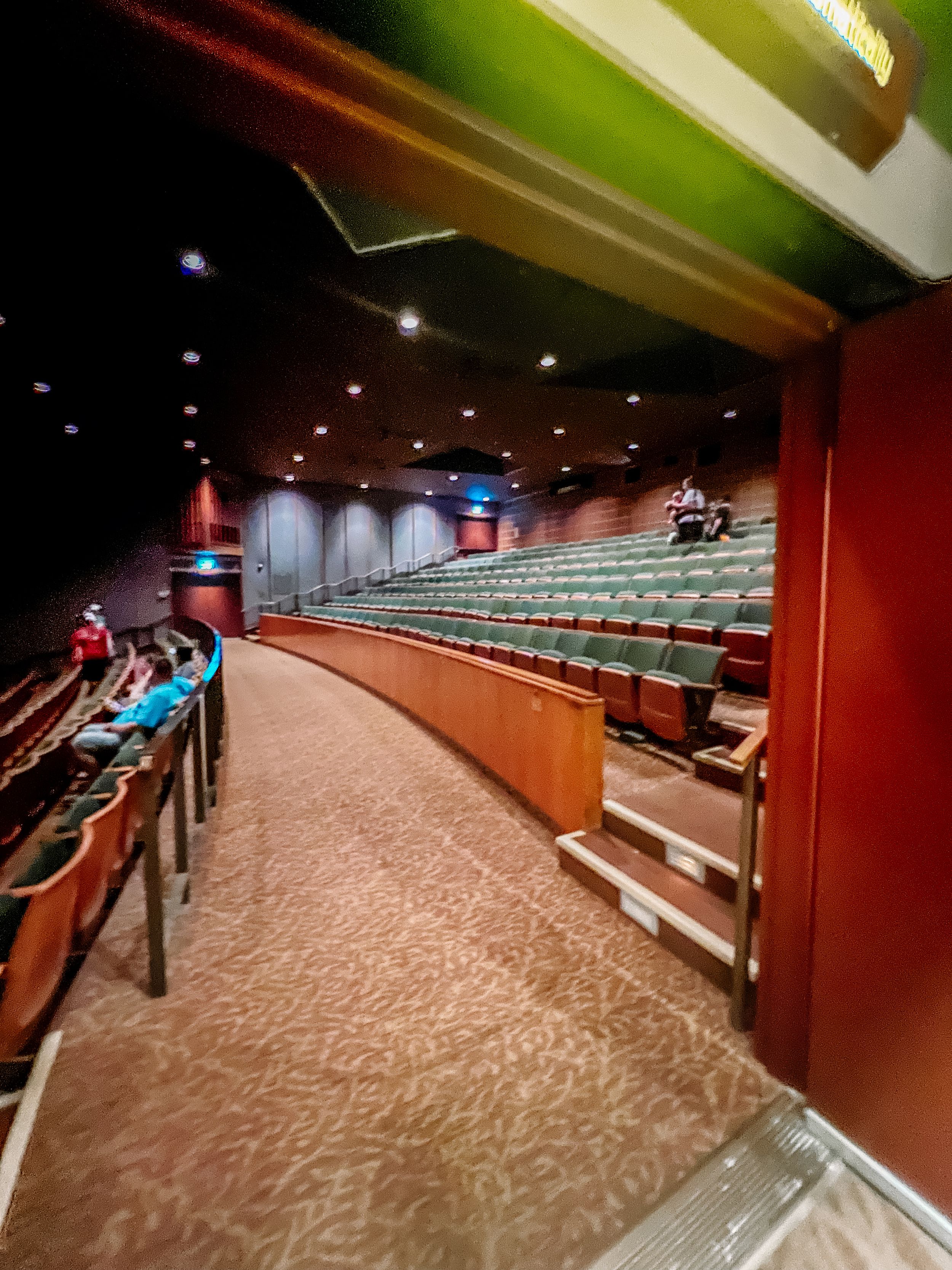 A panoramic view of an auditorium theater interior with curved rows of red seats and carpeted aisles.