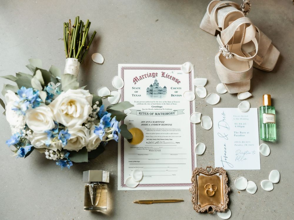 Elegant wedding flat lay with marriage license, bridal bouquet of white and blue flowers, heels, and accessories.