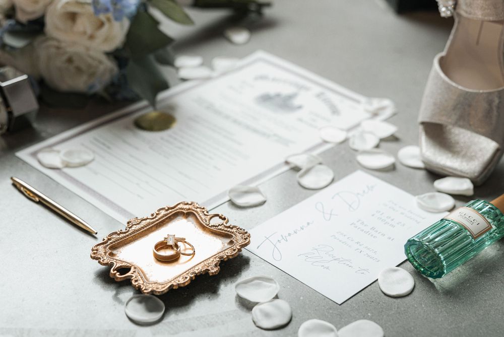 Elegant wedding flat lay featuring gold rings on an ornate tray, invitation suite, and floral accents.