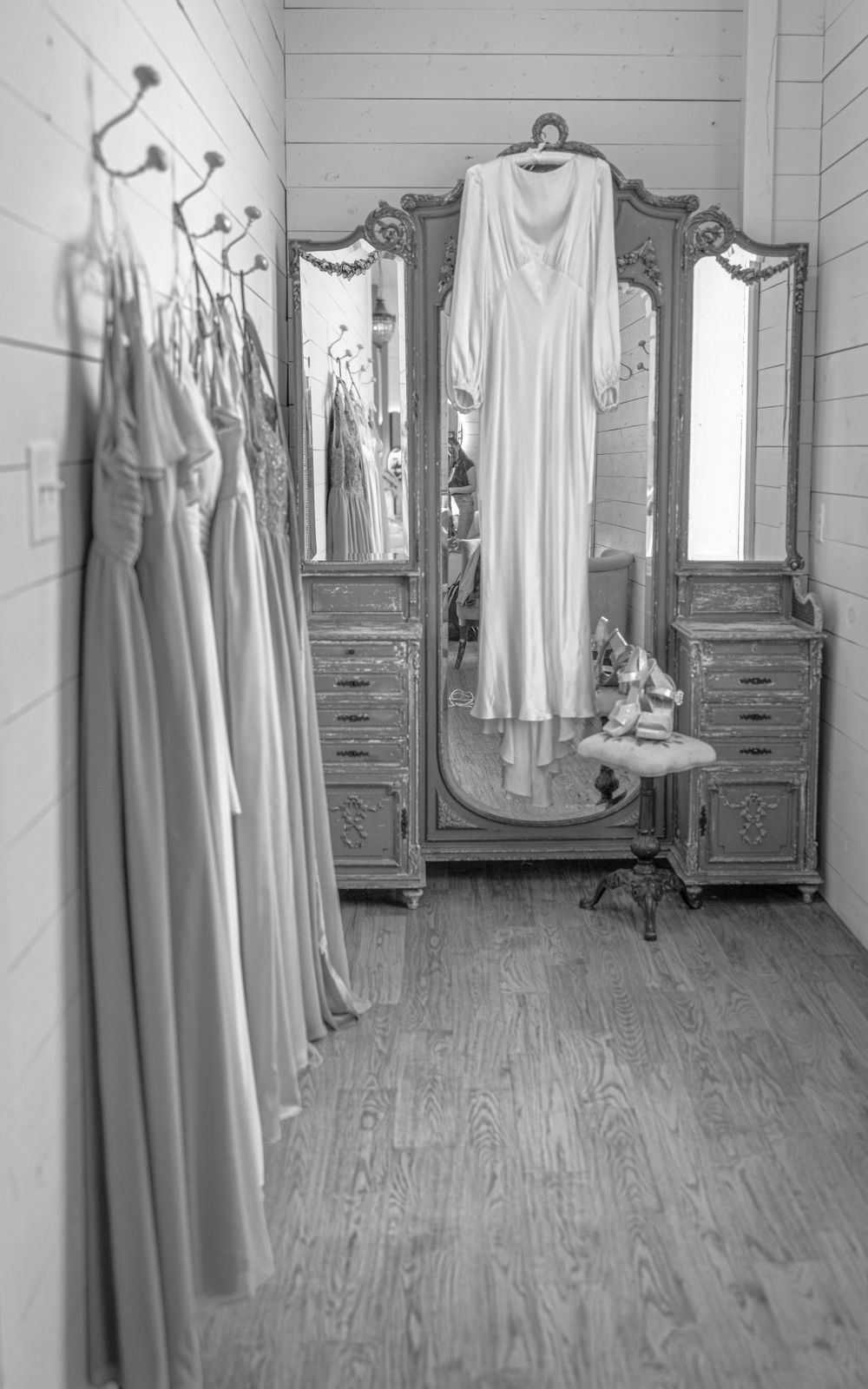 Black and white bridal suite with wedding gown hanging on ornate vintage triple mirror armoire.
