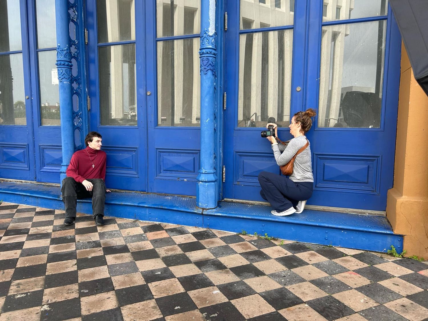 A photographer takes pictures in front of bright blue vintage doorways on a checkered floor entrance.
