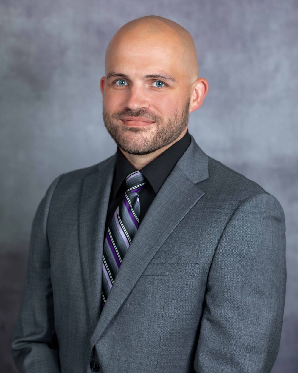 Professional portrait of person wearing dark suit and striped tie in studio setting.