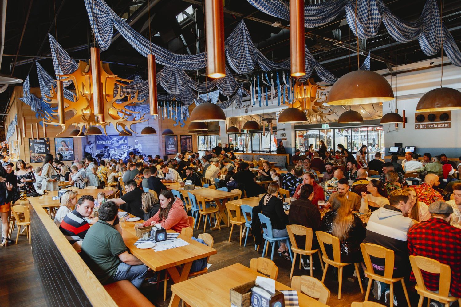 Crowded beer hall with traditional Bavarian blue and white decor filled with patrons at long wooden tables.